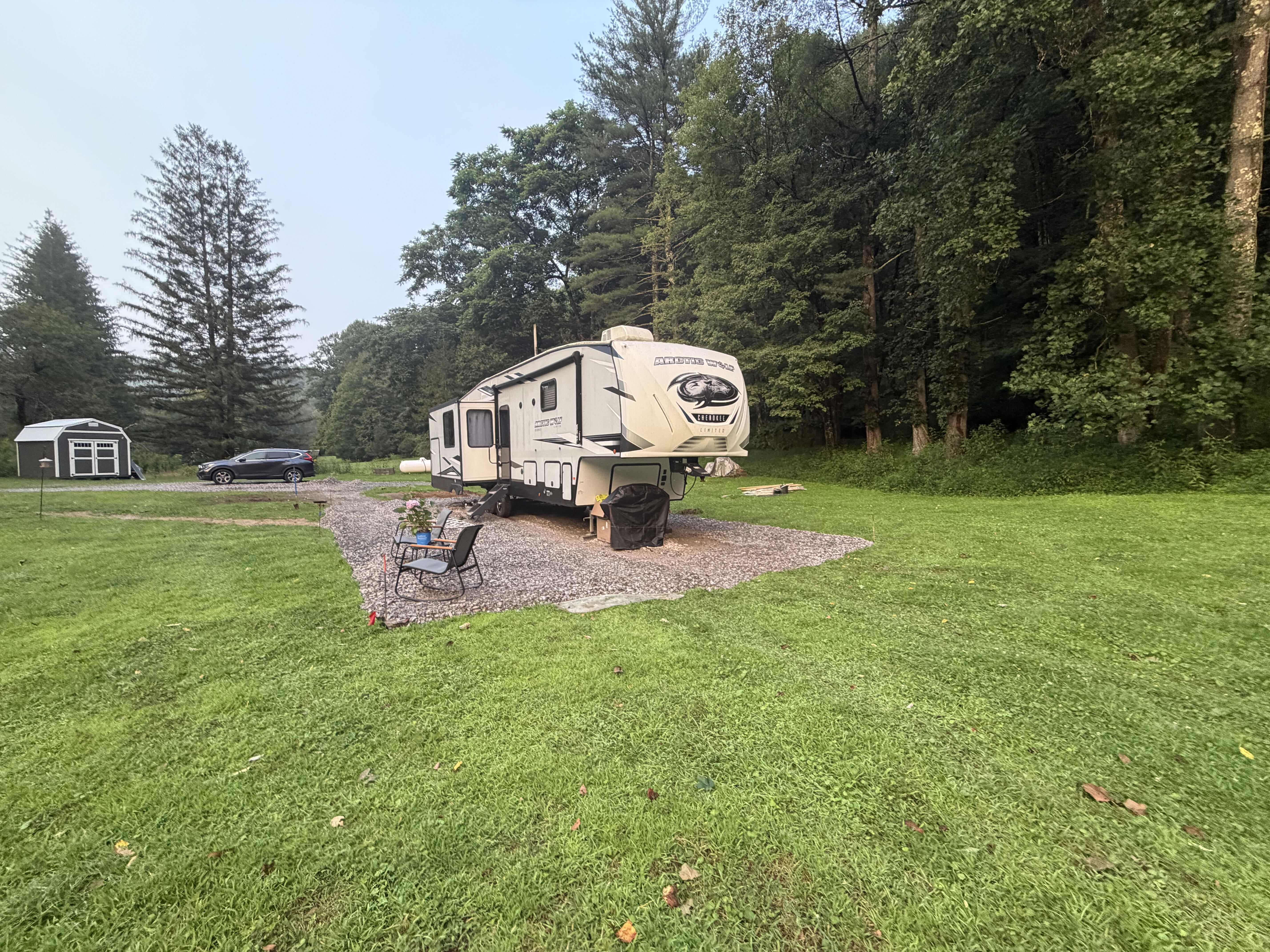 The 5th wheel camper on its gravel pad surrounded by green lawn and trees